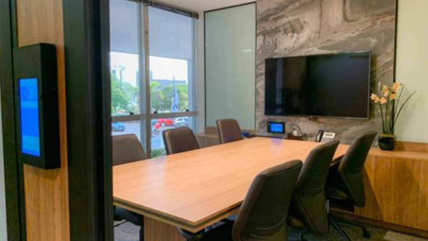Sala de reuniões da unidade de Fortaleza, com mesa de madeira e painel de vídeo