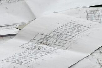 Plantas e desenhos técnicos espalhados sobre mesa, representando processos licitatórios de obras públicas