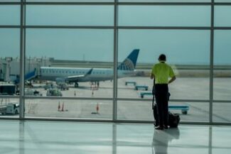 Assessoria para Imigração e Emigração Viajante com mala observando avião pela janela do aeroporto, simbolizando assessoria em imigração e emigração