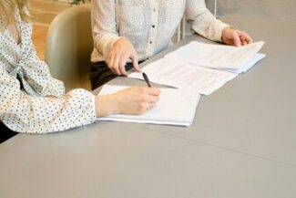 Pessoas assinando documento sobre mesa, simbolizando a formalização de contratos de consumo