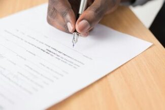 Mão assinando documento sobre mesa de madeira, simbolizando a formalização de testamento