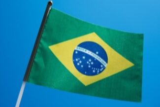 06-naturalizacao-migratorio.jpg Bandeira do Brasil hasteada contra o céu azul, simbolizando a naturalização brasileira