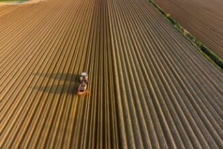 Vista aérea de trator arando campo em linhas organizadas, representando a reestruturação financeira rural