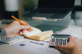 Mãos analisando cálculos com calculadora e caderno, representando análise de dívida e benefícios fiscais