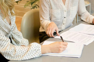 Duas profissionais revisando e assinando documentos contratuais sobre a mesa de reunião