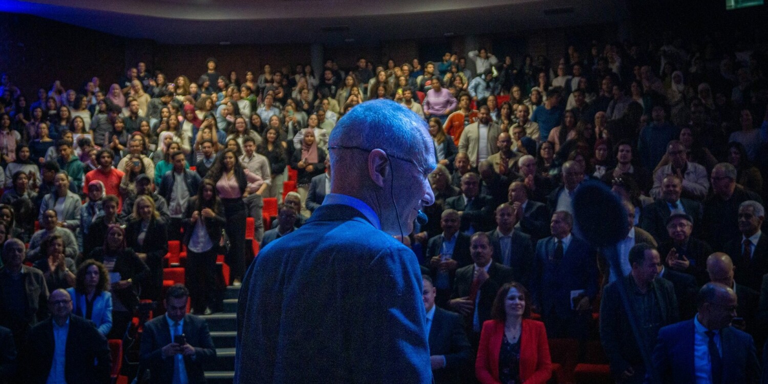 Orador de costas discursa para plateia lotada em auditório
