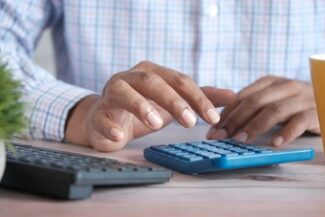 Mãos usando calculadora sobre mesa de trabalho, ao lado de teclado