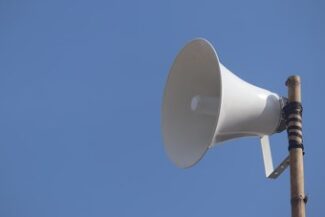 Alto-falante de som branco montado em poste, contra o céu azul